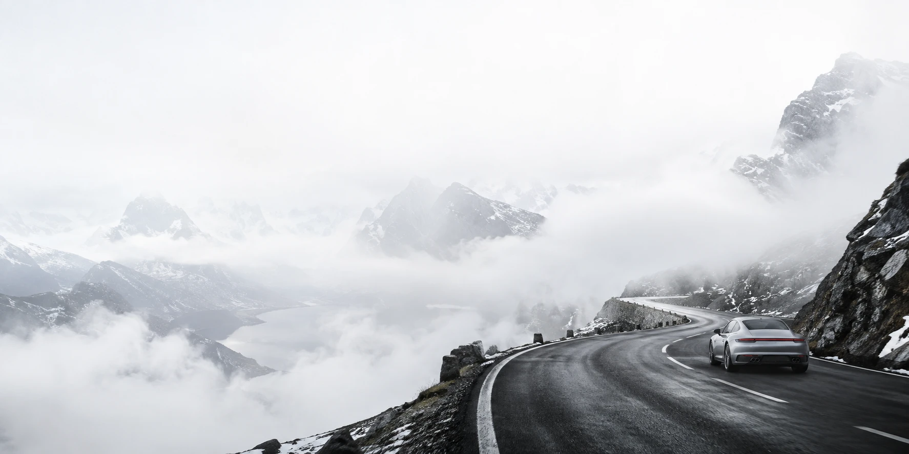 A silver car on an open road through the mountains